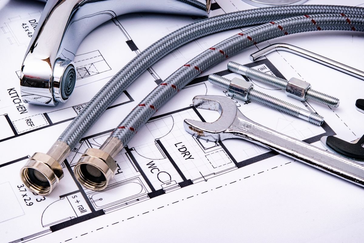 Plumbing tools, braided supply hoses and a faucet arranged on a technical blueprint